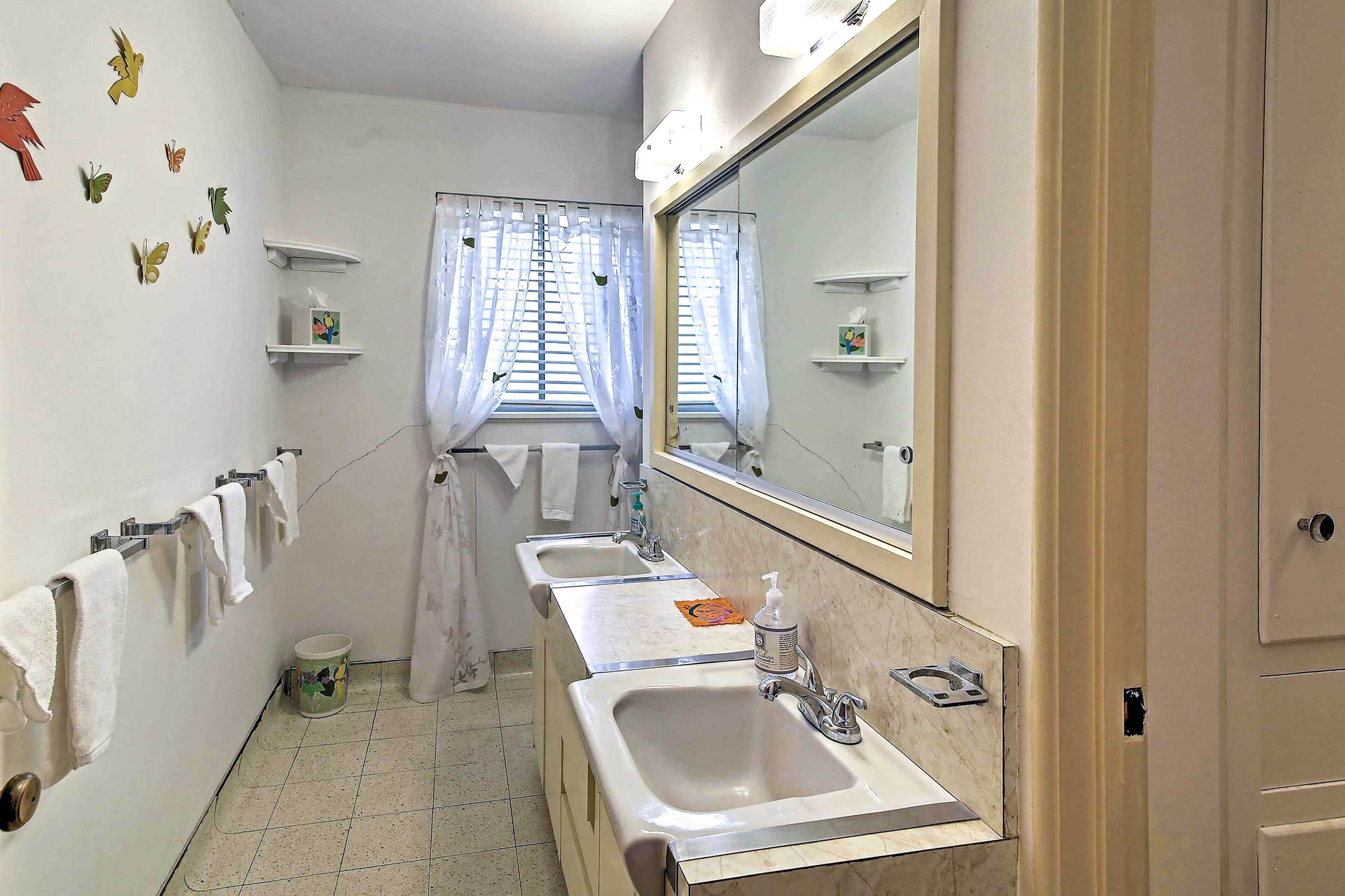 A bathroom with two sinks, a large mirror, and a window with curtains.