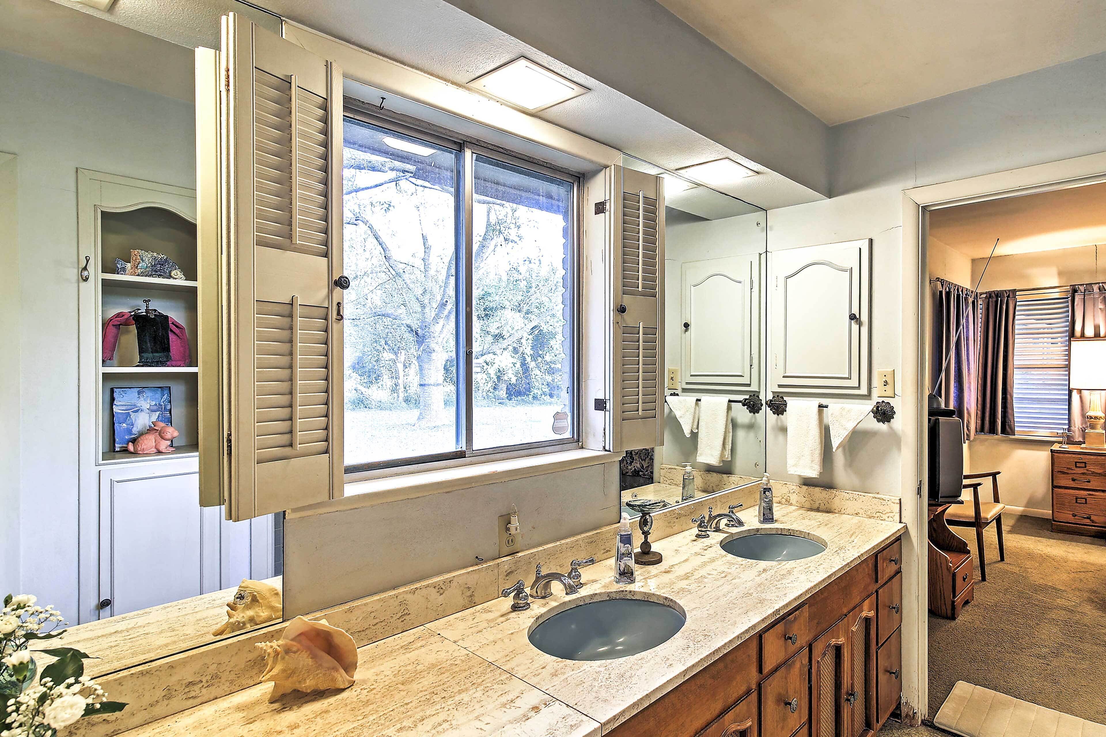 A bathroom with a large window, double sinks, and wooden cabinets.