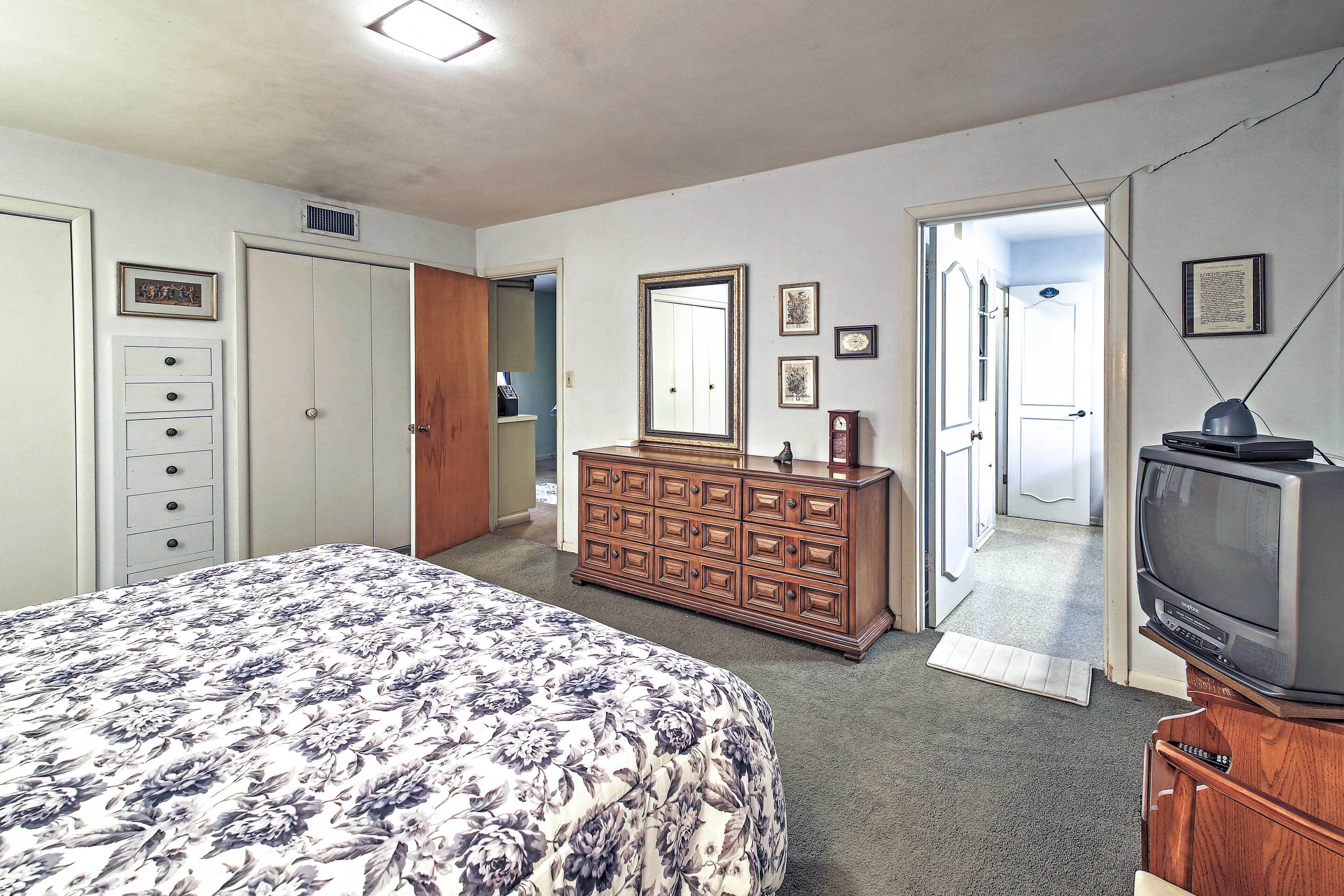 Un dormitorio con cama, cómoda, televisor y una puerta que da a otra habitación.