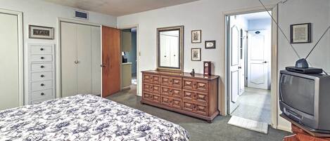 Un dormitorio con cama, cómoda, televisor y una puerta que da a otra habitación.