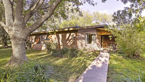 A single-story brick house with a front porch, surrounded by a well-maintained lawn and large trees. - Mid-century Hideaway: Spacious Brownsville Home! (Brownsville)