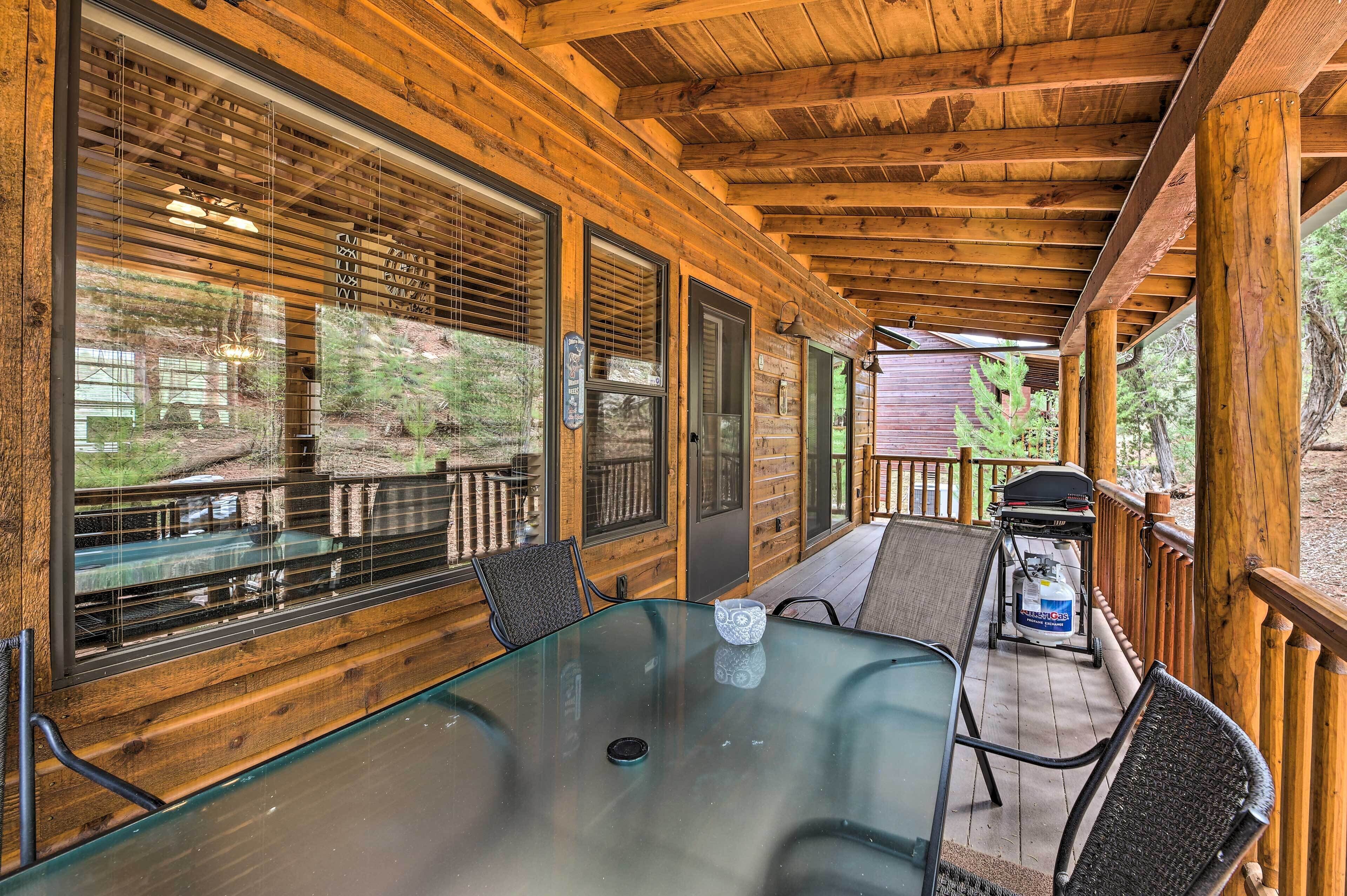 A wooden deck with a glass table and chairs, overlooking a wooded area.