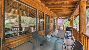 A wooden deck with a glass table and chairs, overlooking a wooded area.