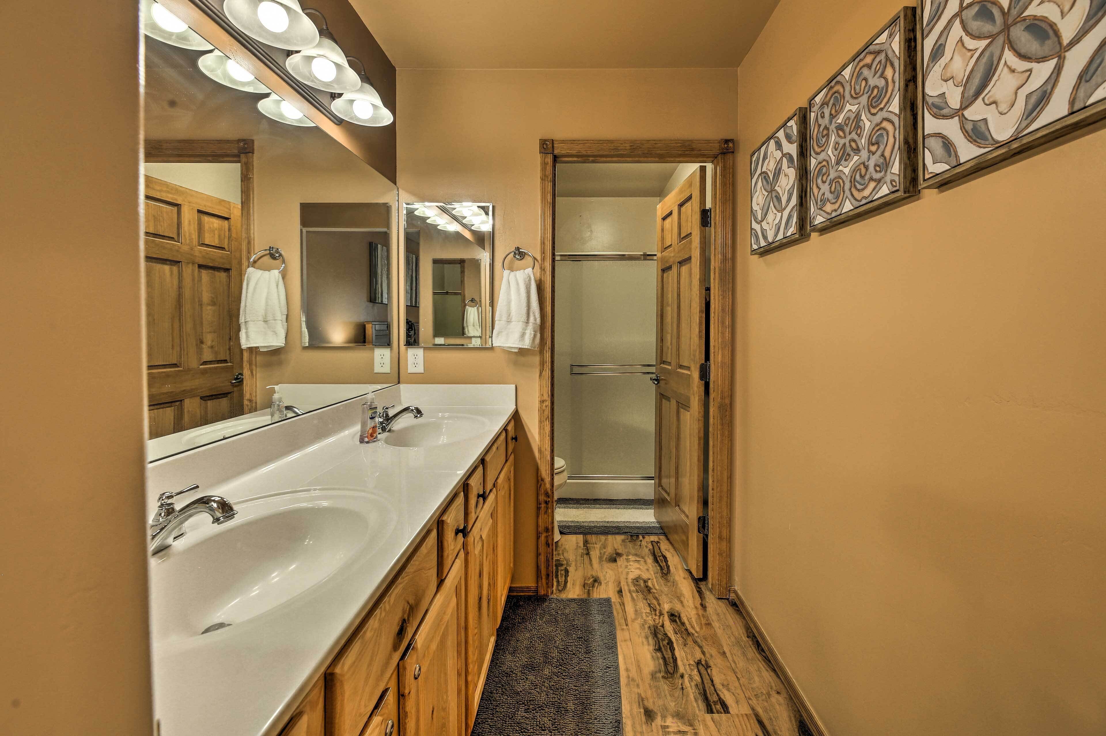 A bathroom with two sinks, a mirror with lights, a shower, and wooden cabinets.