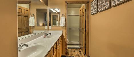 A bathroom with two sinks, a mirror with lights, a shower, and wooden cabinets.