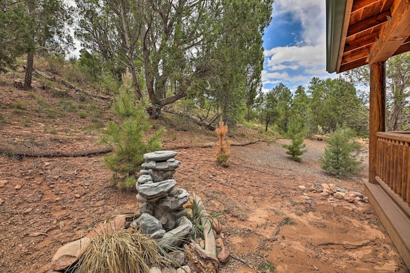 A rustic cabin with a stone structure in the foreground, surrounded by a forested area with a dirt path leading to the cabin. - 3 Mi to Fool Hollow Lake: Cozy Cabin w/ Deck (Show Low)