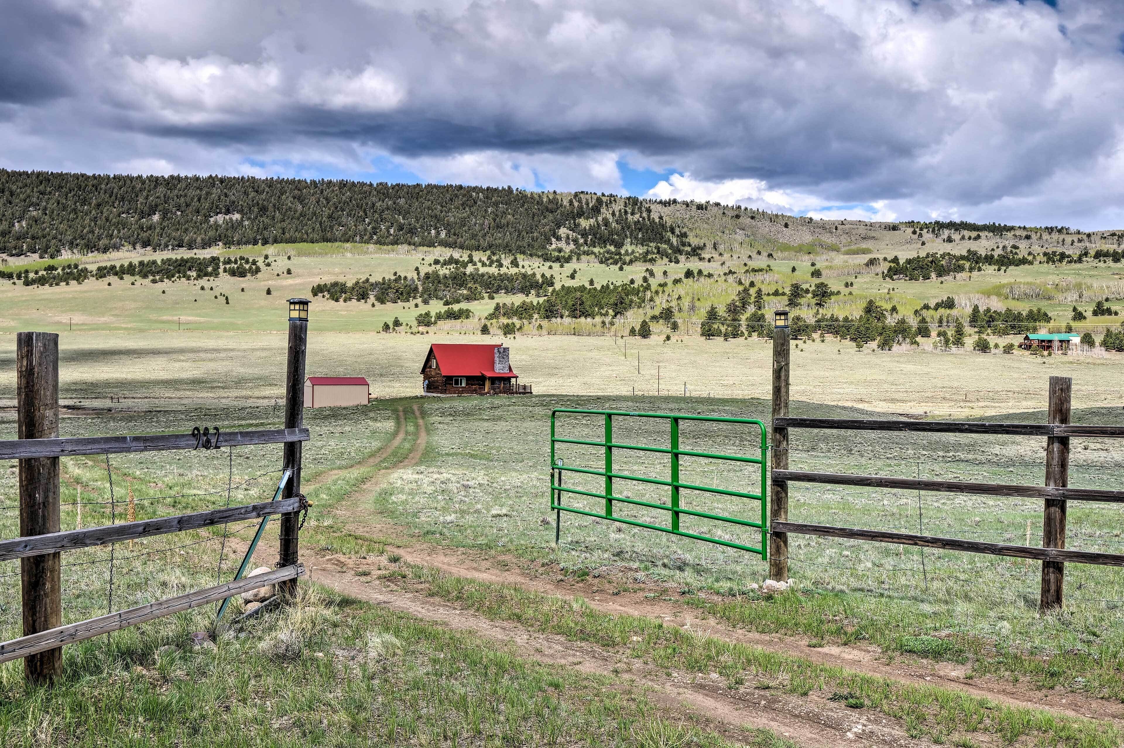 A rural landscape with a wooden fence, a red building, and a green gate.