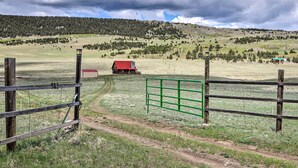Un paysage rural avec une clôture en bois, un bâtiment rouge et un portail vert.