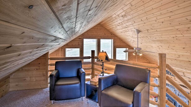 Une pièce mansardée chaleureuse avec des murs en bois et un plafond en pente. On y trouve deux fauteuils en cuir, une petite table avec une lampe et une fenêtre donnant sur un beau paysage.