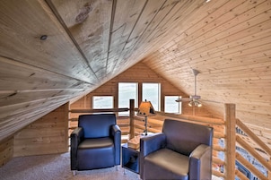 Una habitación acogedora en el ático, con paredes de madera y techo inclinado. Hay dos sillones de cuero, una mesita con una lámpara y una ventana con vistas.