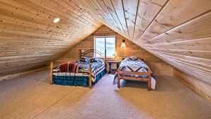 Une chambre mansardée chaleureuse avec deux lits en bois, une fenêtre et une lampe.