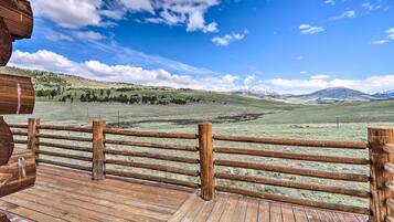 A wooden deck with a wooden fence overlooking a grassy field with distant mountains.