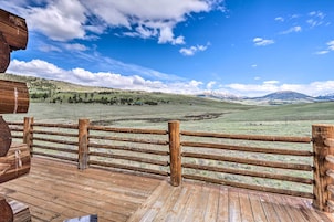 Una terraza de madera con cerco de madera da a un campo cubierto de hierba y montañas al fondo.