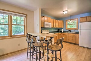 Una cocina con armarios de madera, un refrigerador blanco, un microondas y un comedor con taburetes.