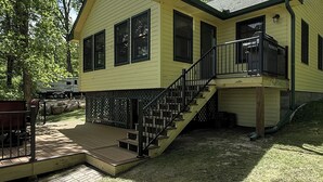 Une maison jaune avec une terrasse en bois, un escalier et un garage fermé.