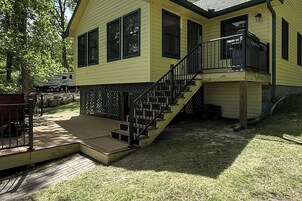 Una casa amarilla con terraza de madera, escaleras y garaje cubierto.
