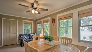 Une salle à manger avec une table en bois, des chaises, un ventilateur de plafond et des fenêtres équipées de stores.