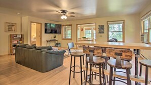 Un salon spacieux avec un grand canapé, un coin repas avec une longue table et des tabourets de bar, et un ventilateur de plafond.