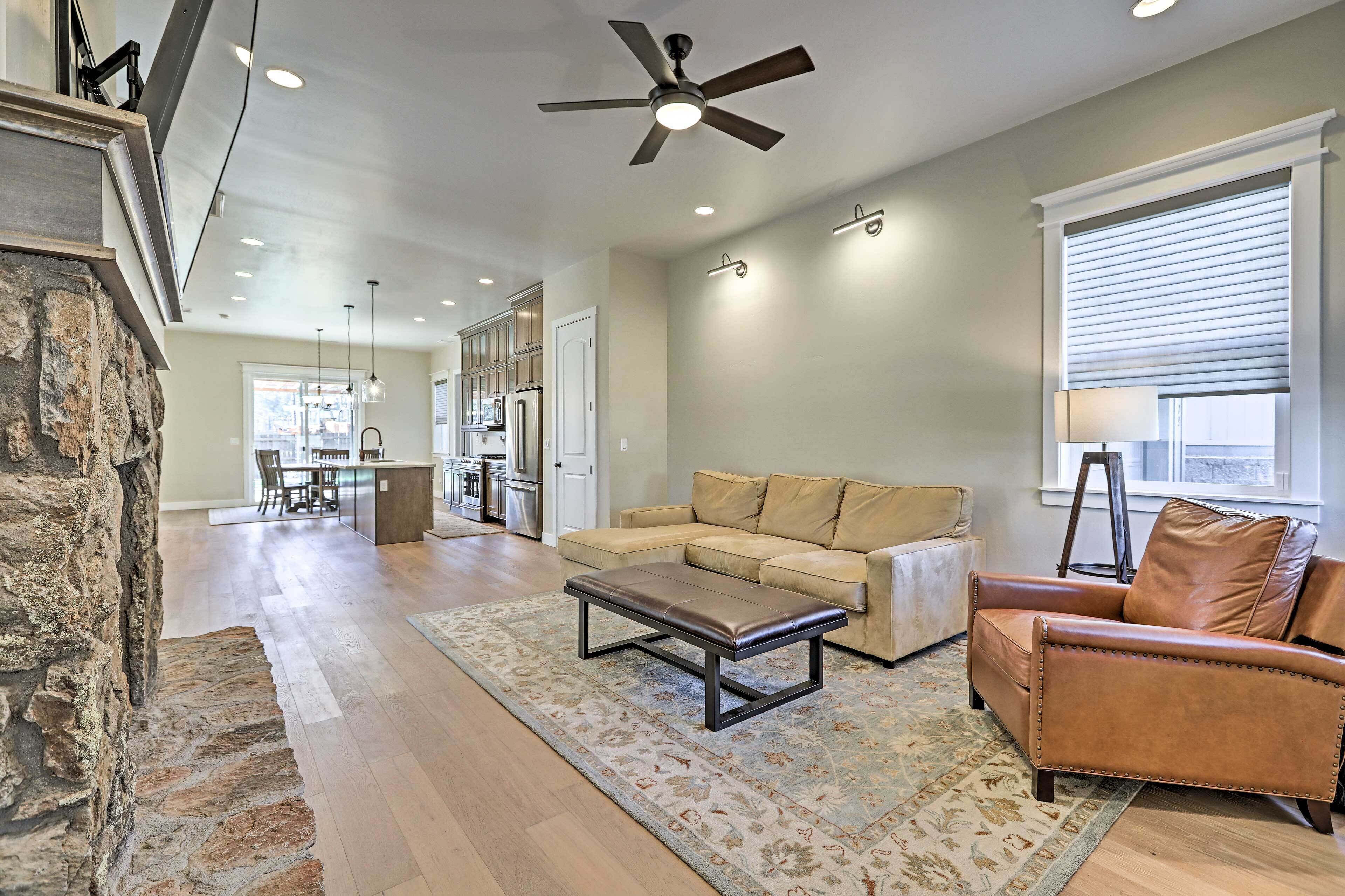 A spacious living room with a stone accent wall, a ceiling fan, a leather sofa, a coffee table, and a large window with blinds.