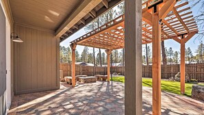 A covered patio area with a wooden pergola, stone flooring, and a view of a fenced yard with trees. - Flagstaff Oasis w/ Hot Tub - 3 Mi to Downtown! (Flagstaff)
