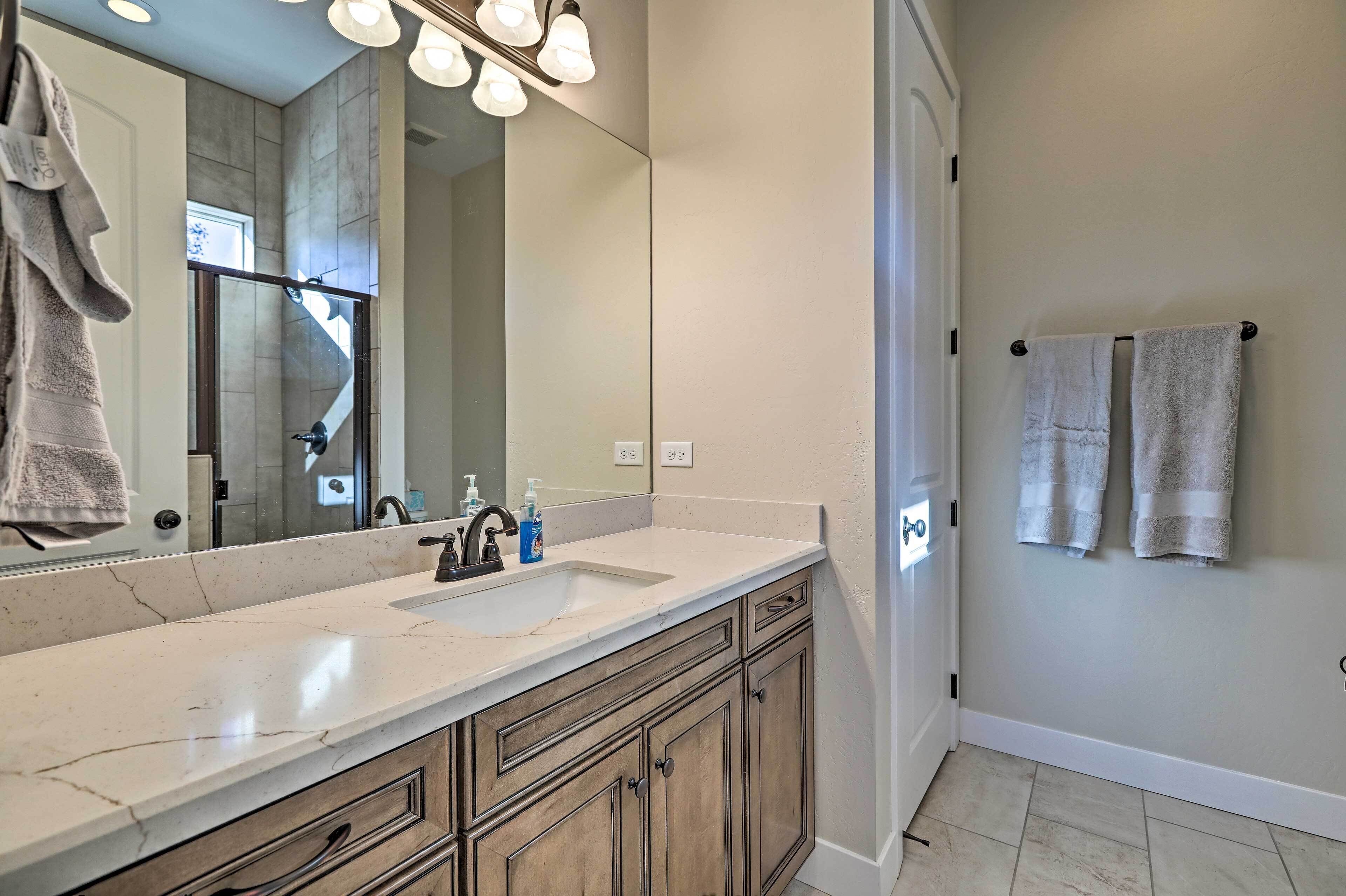 A bathroom with a marble sink, wooden cabinets, a large mirror, and two towels hanging on a rack.