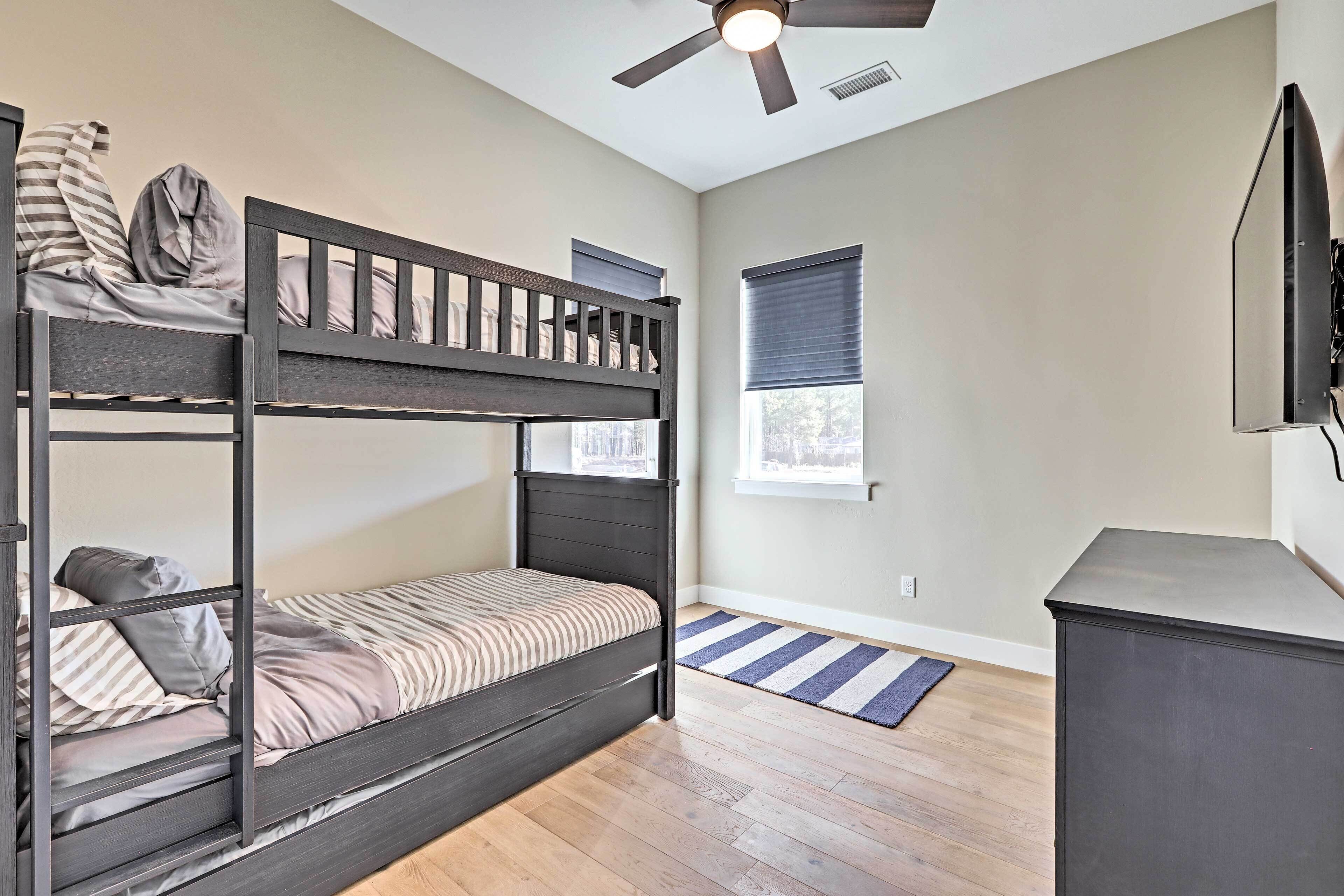 A room with a bunk bed, a desk, a ceiling fan, a window, and a door.