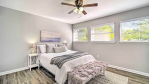 A bedroom with a bed, a ceiling fan, a nightstand, a bench, and three windows with blinds. - Coldspring Cottage < 1 Mi to Lake Livingston! (Coldspring)
