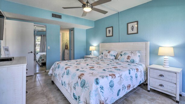 A bedroom with a bed, two bedside tables, a ceiling fan, and a door leading to another room. - Sweet Snowbird Escape ~ 2 Mi to St Pete Beach (St. Petersburg)