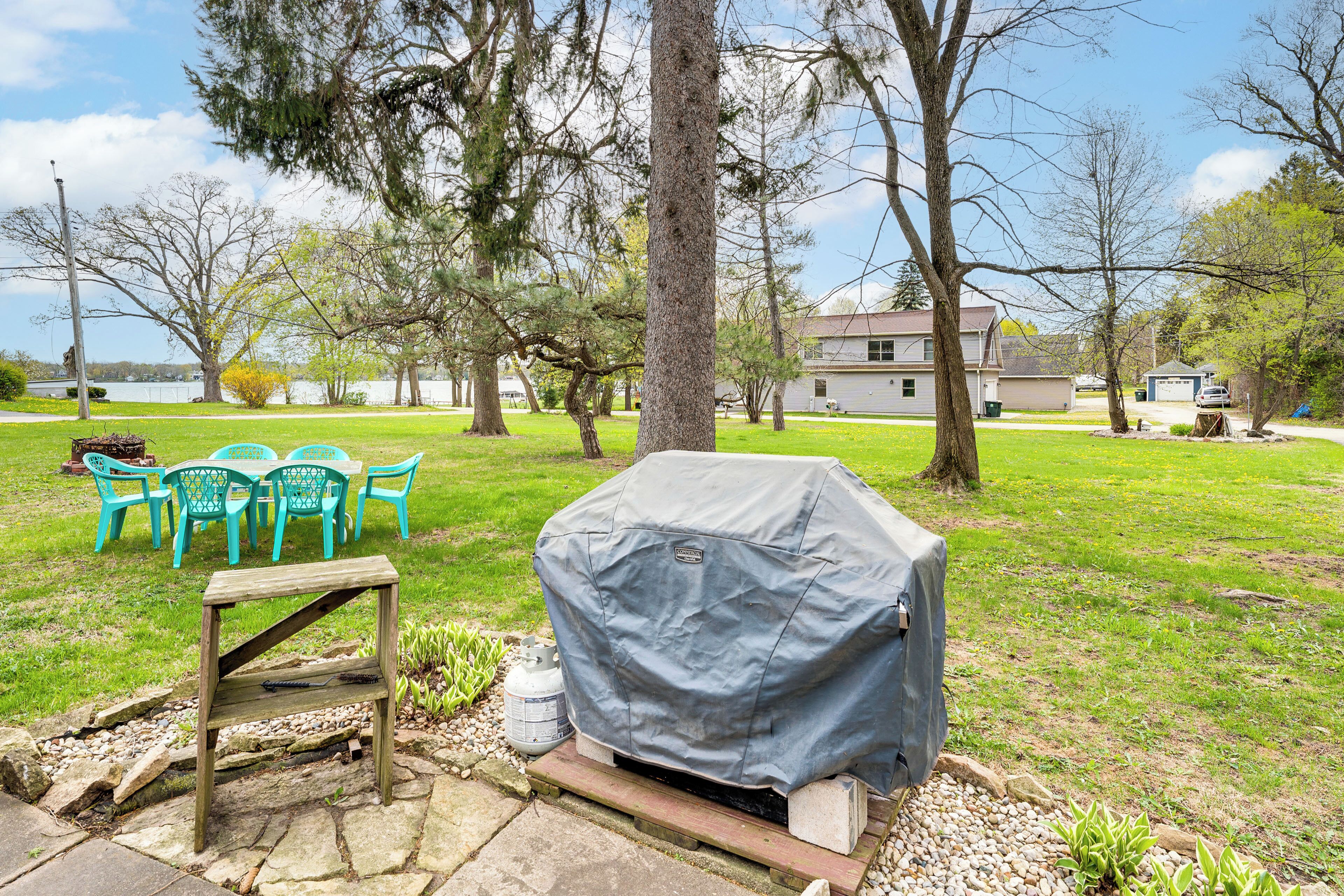 A backyard with a barbecue grill, outdoor furniture, and a view of a lake and houses in the background.