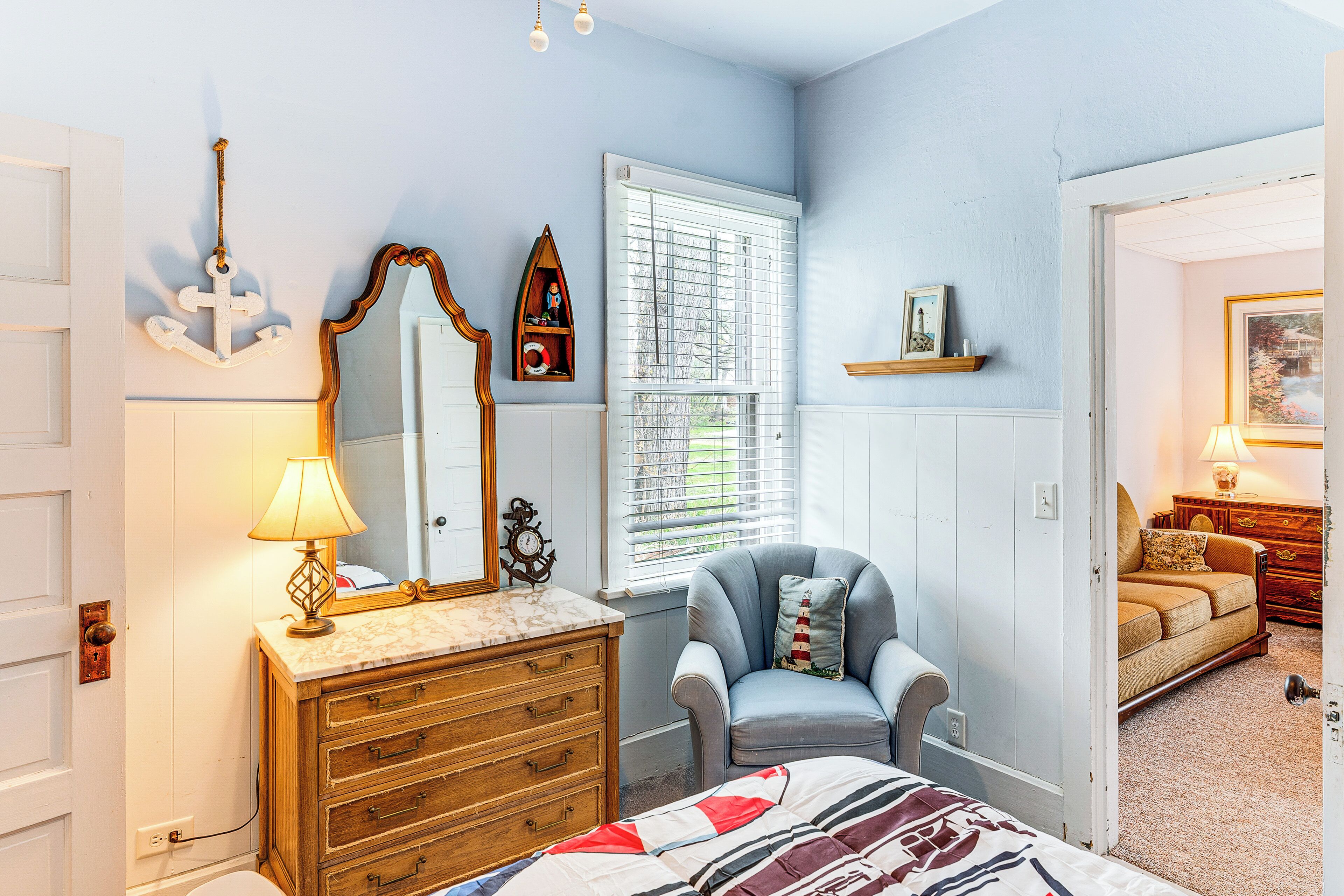 Een slaapkamer met een bed, dressoir, stoel en een raam met jaloezieën.