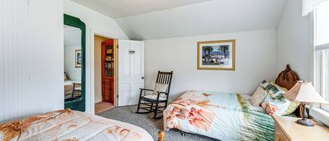 Un dormitorio con dos camas, un aparador de madera, una mecedora y un cuadro enmarcado en la pared.