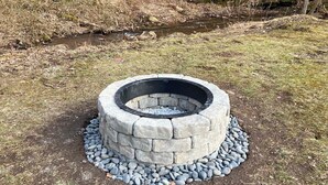 En stenfyrsted med cirkulært stendekor og metal kant, omgivet af en stenmur og et lag flade sten.
