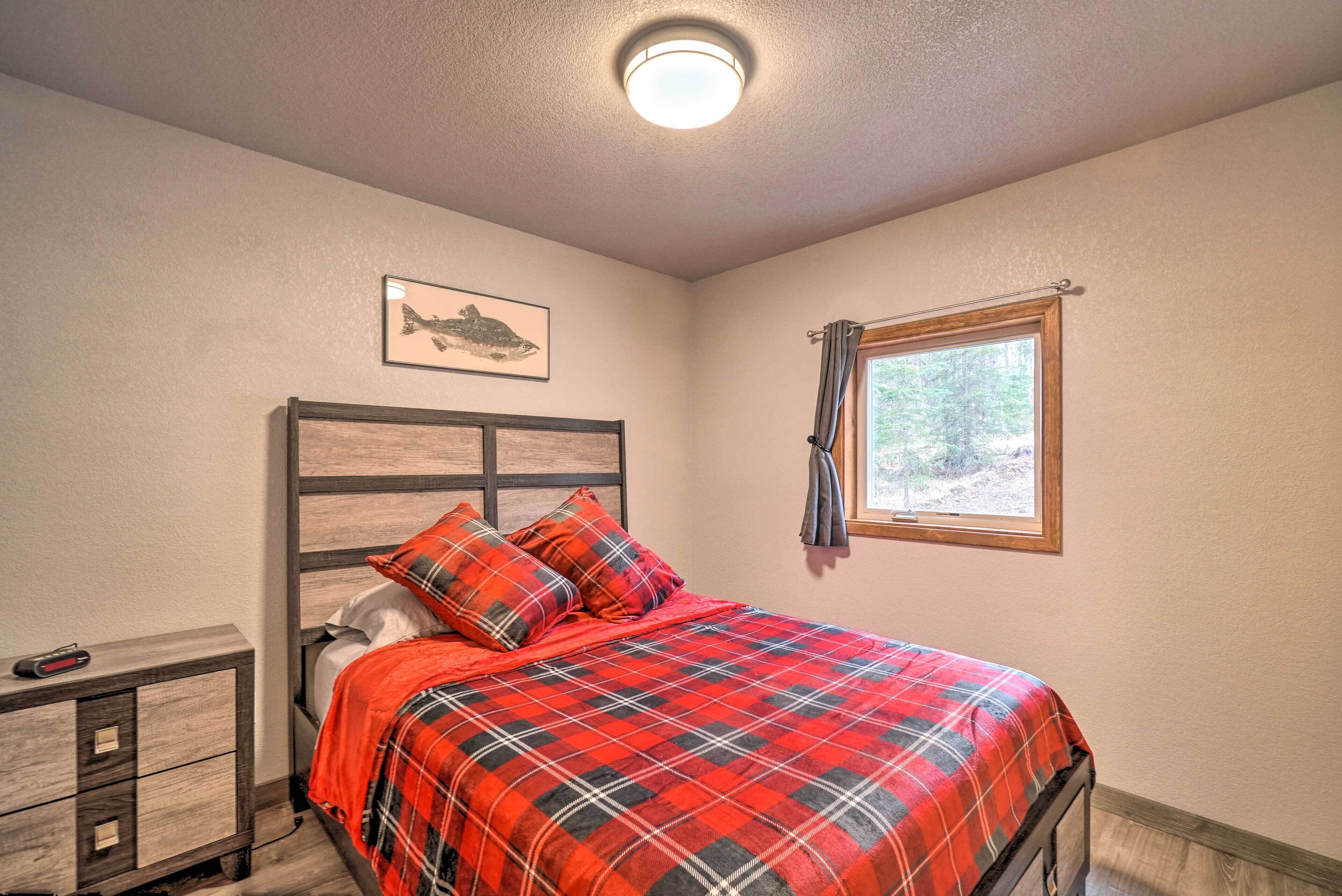 Quarto com cama, mesa de cabeceira, quadro e janela com vista para árvores.