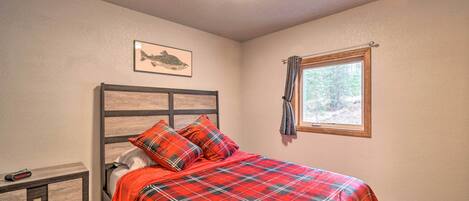 Quarto com cama, mesa de cabeceira, quadro e janela com vista para árvores.