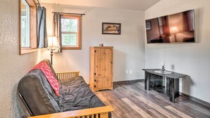 A cozy room with a dark-colored sofa, a wooden cabinet, a small table with a lamp, and a flat-screen TV mounted on the wall.