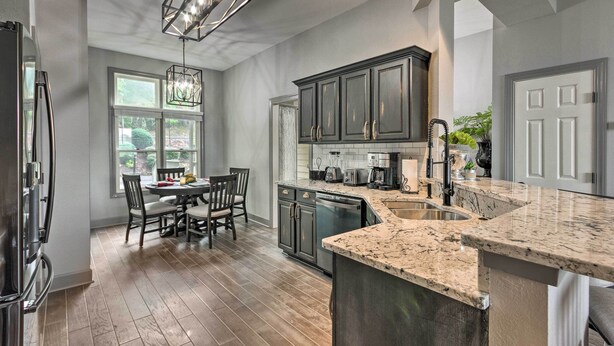A modern kitchen with dark cabinets, a granite countertop, and a dining area with a table and chairs. - Surrounding Mtn Views! Modern Smokies Retreat (Burnsville)