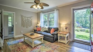 Un salon avec un canapé, une table basse et un ventilateur de plafond. Il y a une fenêtre avec des rideaux et une vue sur l’extérieur.
