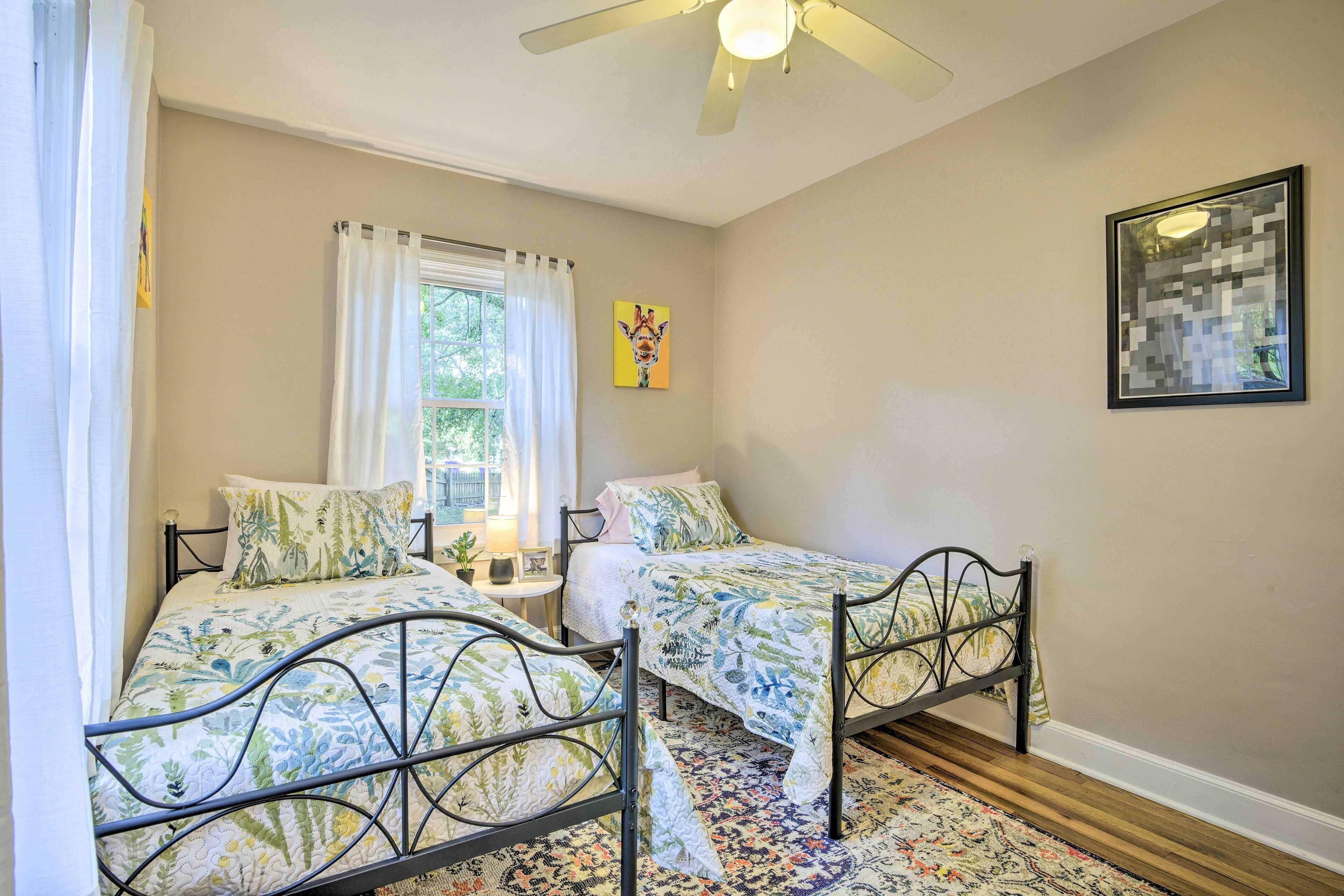 A bedroom with two beds, a ceiling fan, a window with curtains, and a framed picture on the wall.