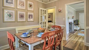 Une salle à manger avec une table en bois, des chaises, des tableaux représentant des marchés aux fleurs et un lustre.
