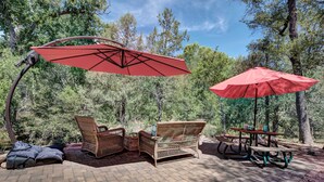 An outdoor patio with wicker furniture, red umbrellas, and picnic tables. - Tonto Nat'l Forest Riverside Cabin! (Payson)