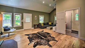 Ein geräumiges Wohnzimmer mit Holzdielenboden, einem großen schwarzen Lederteppich, einem grauen Sofa mit gelben Kissen und einem weißen Sessel.