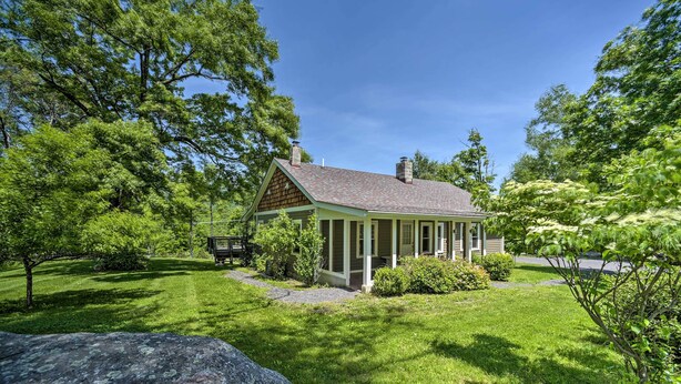 Ein eingeschossiges Haus mit Satteldach, umgeben von üppigen, grünen Bäumen und einem gepflegten Rasen.