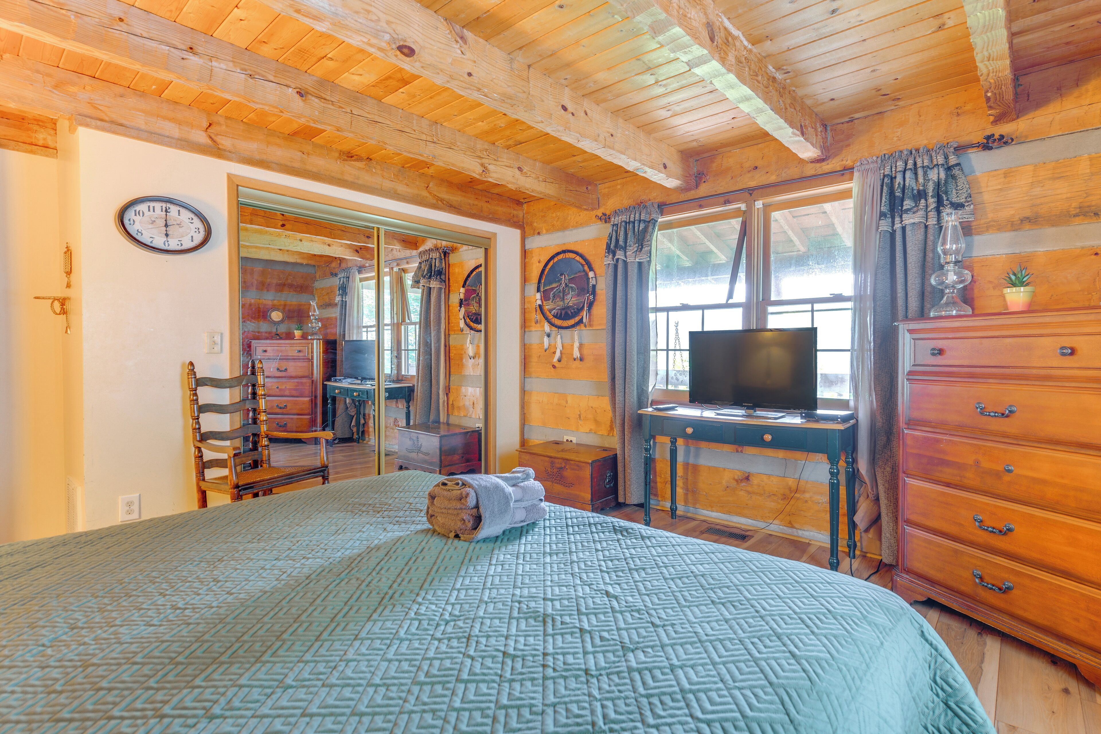 A wooden cabin room with a bed, a dresser, a television, and a window with curtains.