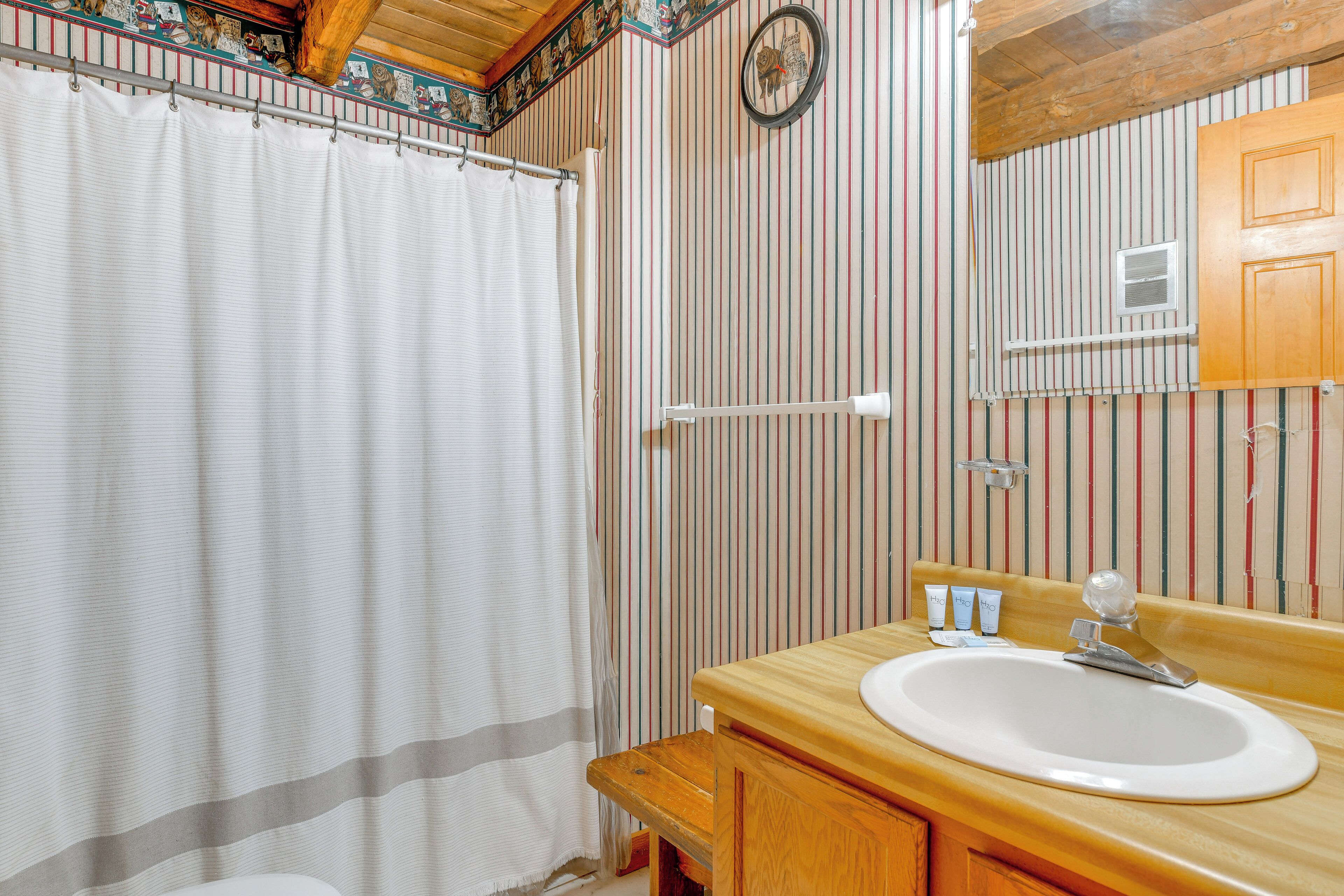 Une salle de bain avec un mur à rayures, un meuble-lavabo en bois, un lavabo blanc et un rideau de douche.