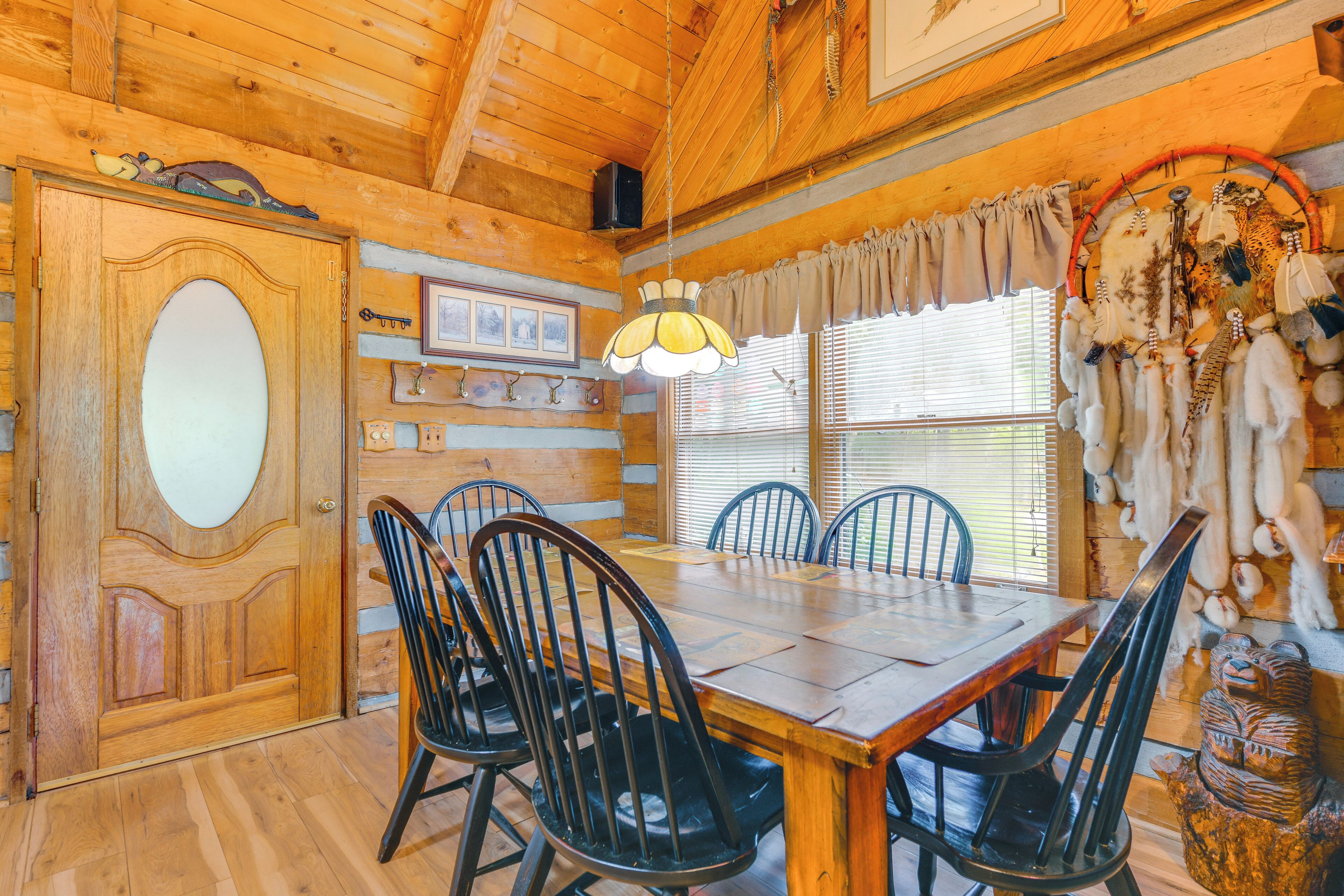 A wooden interior with a dining table, chairs, a large wooden door, and a wall with mounted items.