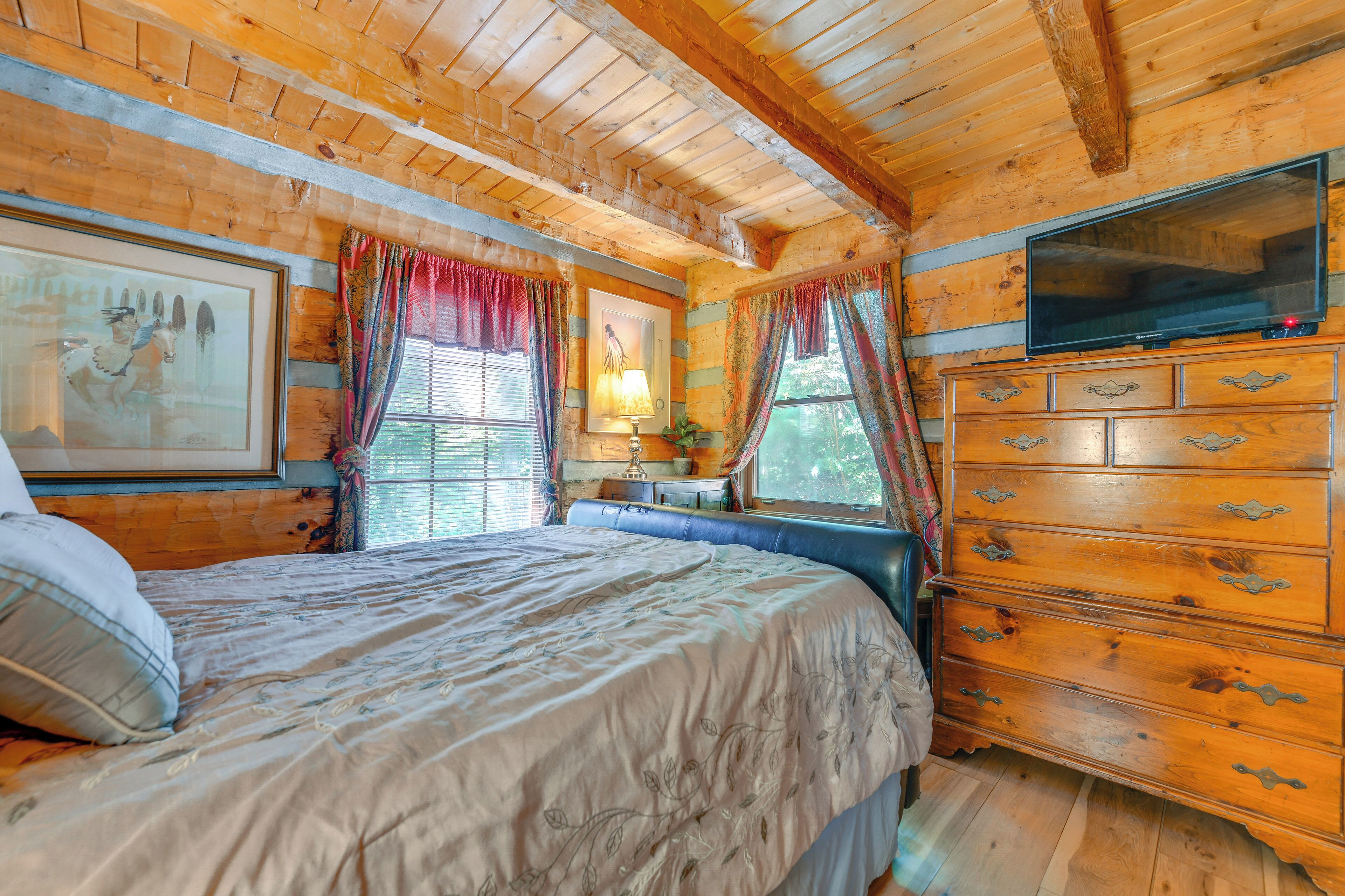 A wooden cabin bedroom with a bed, dresser, and TV.