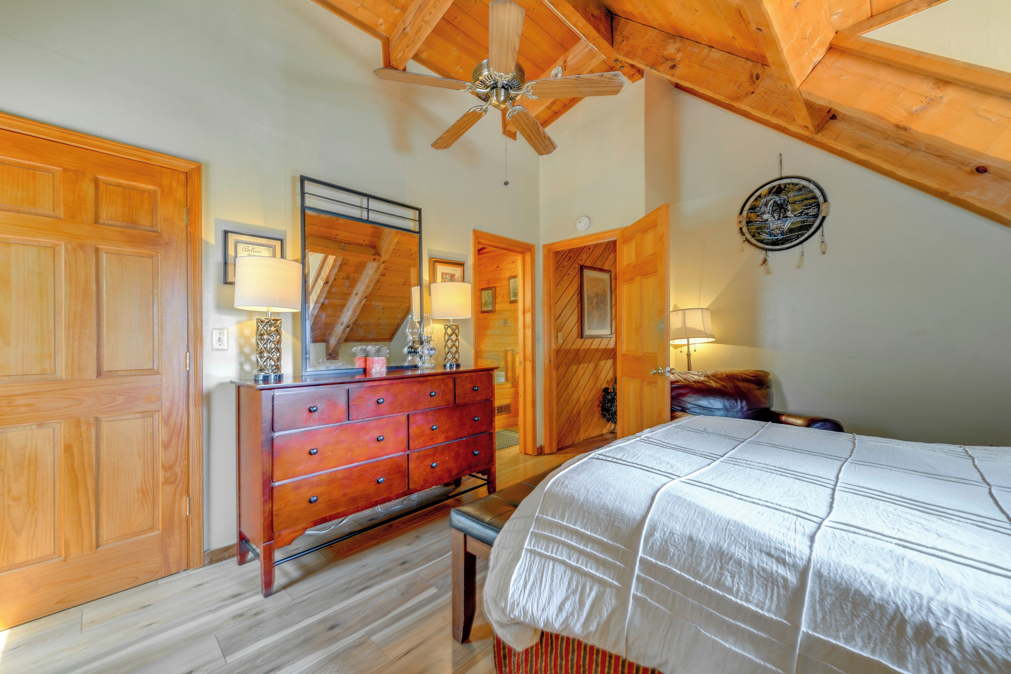 A bedroom with a wooden ceiling, a bed with a white bedspread, a wooden dresser, and a ceiling fan.