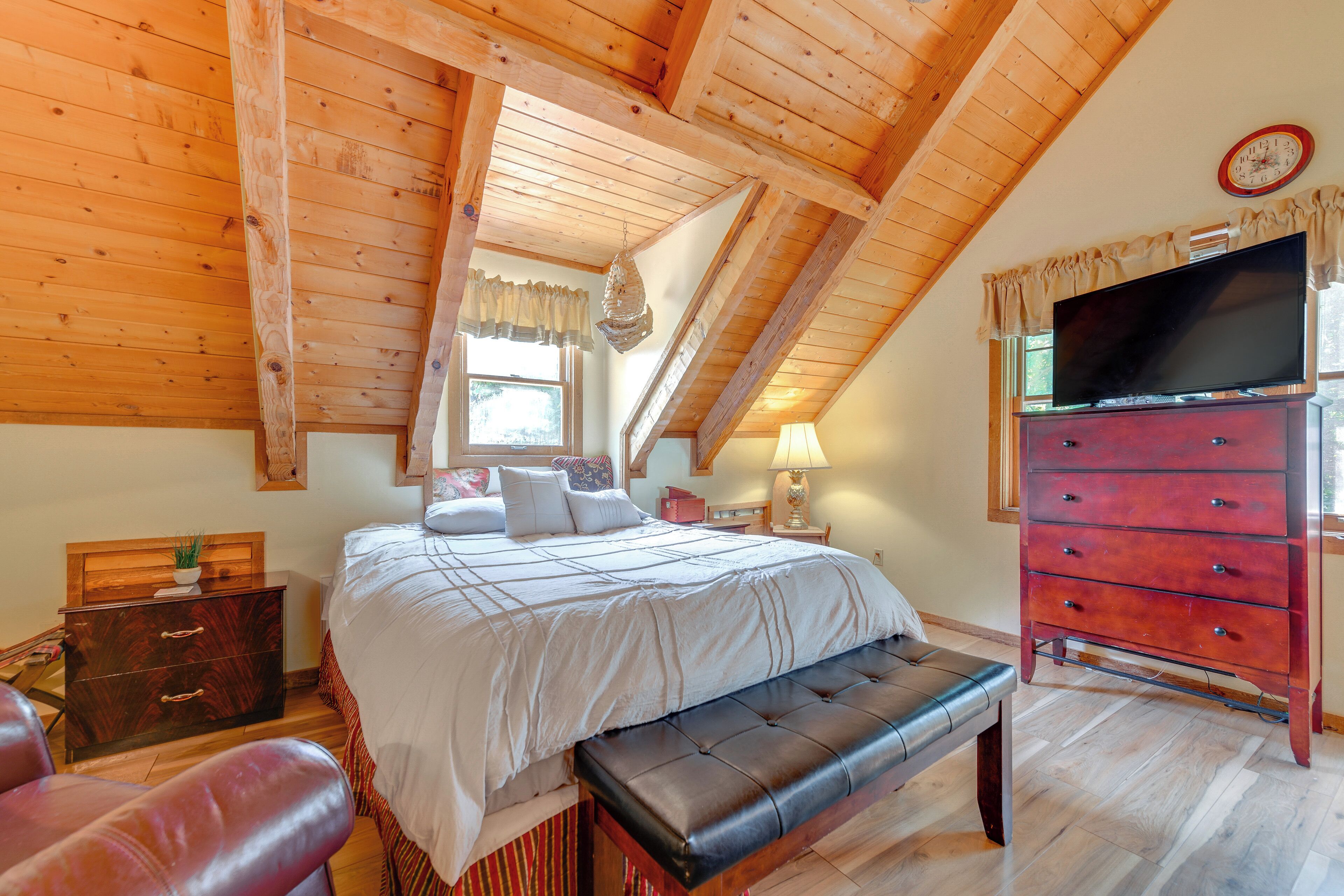 Camera da letto con soffitto in legno, un letto con biancheria bianca, una panca, un comò e una televisione.
