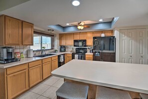 A modern kitchen with wooden cabinets, a central island, a microwave, a refrigerator, and a ceiling fan. - 2 Mi to Dtwn: Lake Havasu City Oasis w/ Pool (Lake Havasu City)
