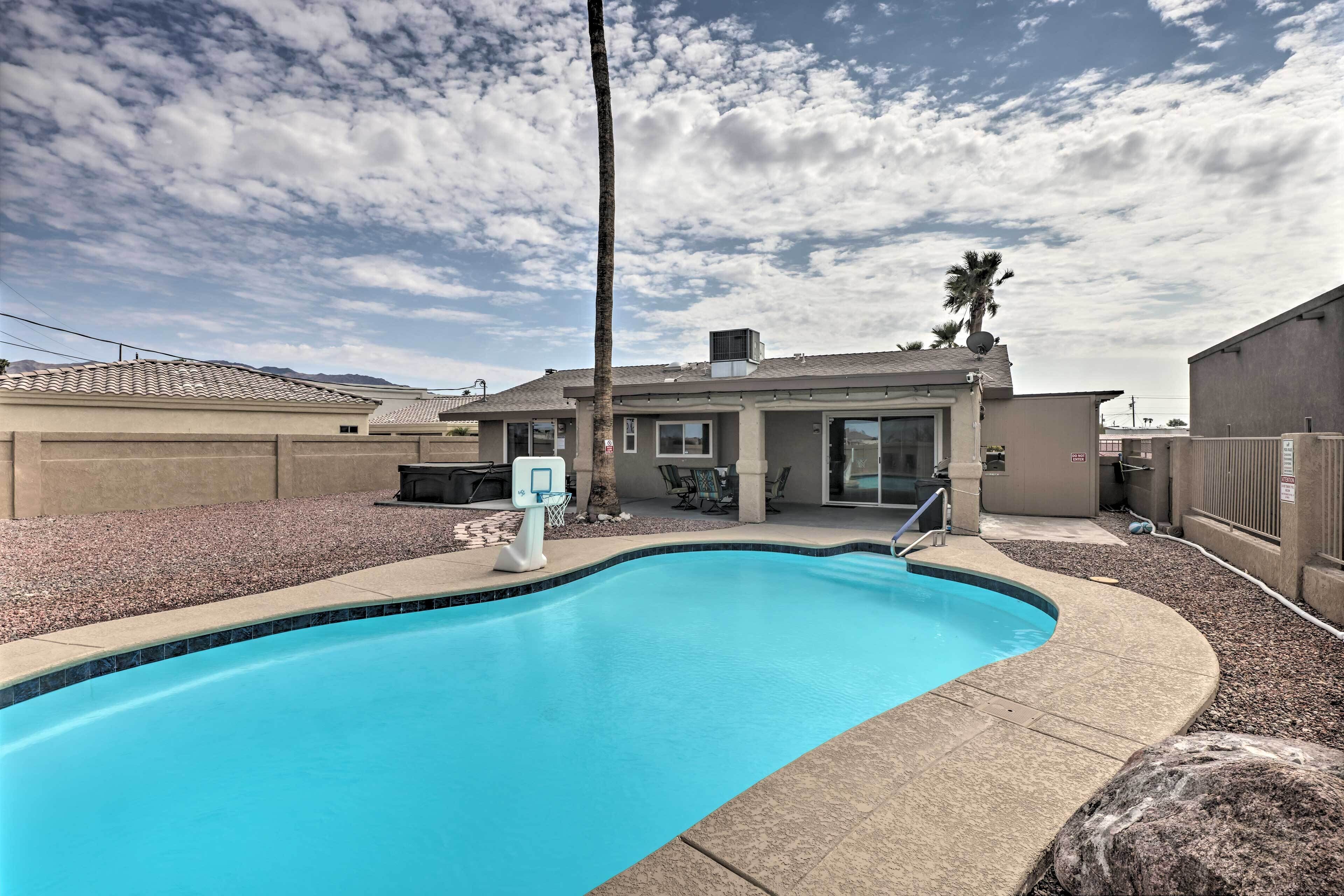 A swimming pool with a basketball hoop, surrounded by a patio area with outdoor furniture and a palm tree.